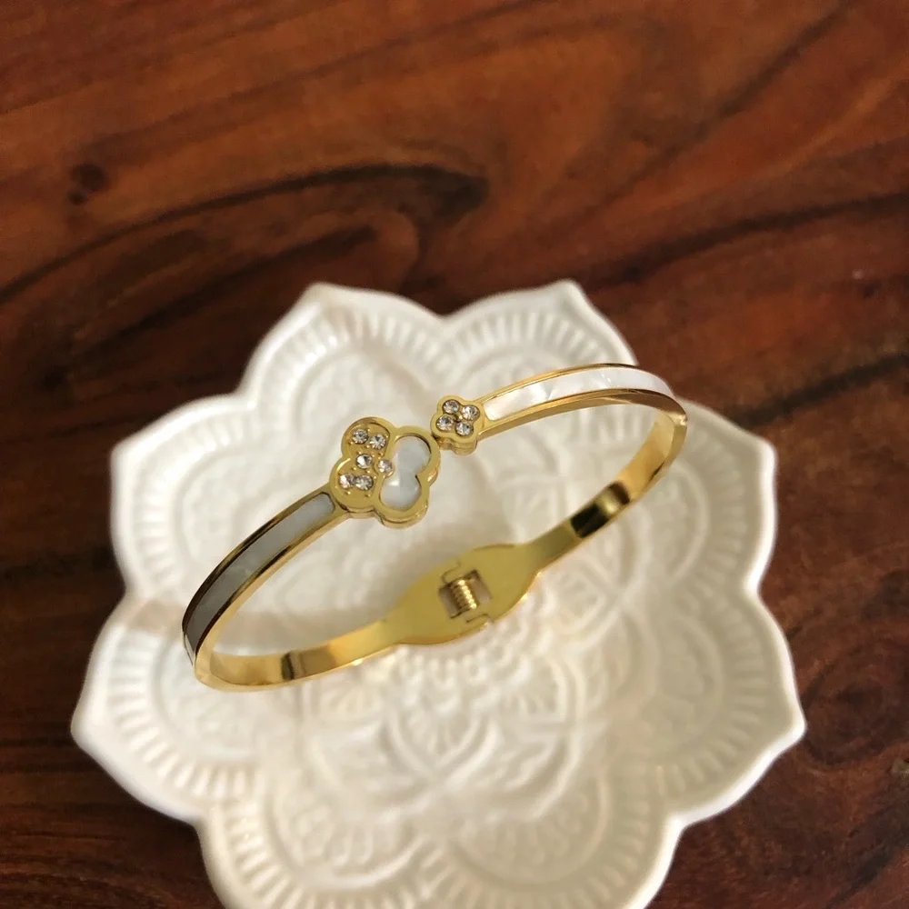 gold-toned hinged bangle bracelet featuring white clover motifs and crystal New